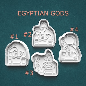 May include: Four white plastic cookie cutters in the shapes of Egyptian gods. The text "EGYPTIAN GODS" is above the cookie cutters. Each cutter is numbered from 1 to 4. The background is a teal color.