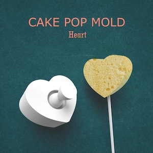 May include: A white heart-shaped cake pop mold with a matching cake pop on a stick. The cake pop is yellow and has a textured surface. Text on the image reads "CAKE POP MOLD Heart".