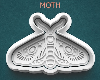 May include: White moth-shaped cookie cutter with intricate details, including stars and circles, against a teal background. The word "MOTH" is printed in orange above the cutter. This item is ideal for baking.