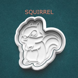 May include: White plastic squirrel-shaped cookie cutter with the word "SQUIRREL" in orange text above. The cutter has a detailed design of a squirrel with a fluffy tail and is set against a teal background.