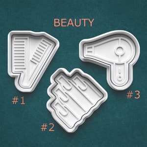 May include: White plastic cookie cutters in the shape of beauty tools. The image includes a comb, a hair dryer, and a set of nail polish bottles. The word "BEAUTY" is printed in orange at the top of the image. Numbers are printed below each cutter.