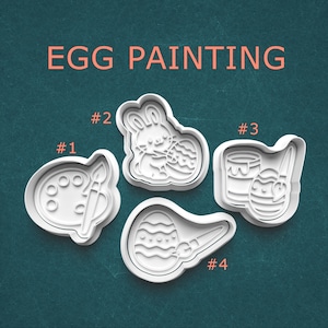 May include: Four white plastic Easter-themed cookie cutters. The cutters include a paint palette with a brush, a bunny with an egg, a paint can with an egg and brush, and an egg with a brush. The text "EGG PAINTING" is at the top.