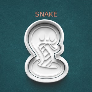 May include: White plastic cookie cutter shaped like a snake with the word "SNAKE" above it.