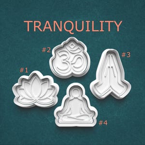 May include: Four white cookie cutters with a yoga and meditation theme. The shapes include a lotus flower, the Om symbol, praying hands, and a seated figure. The word "TRANQUILITY" is printed in orange above the cookie cutters.