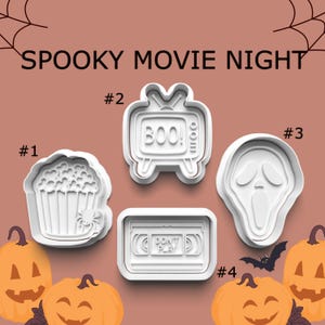 May include: White plastic cookie cutters in the shapes of popcorn, a television with "BOO!" on the screen, a ghost face, and a VHS tape with "DON'T PLAY" on it. The words "SPOOKY MOVIE NIGHT" are at the top.