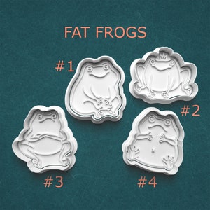 May include: Four white plastic cookie cutters shaped like frogs. The cutters are numbered 1 through 4. The text "FAT FROGS" is at the top of the image.