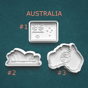 May include: Three white cookie cutters with an Australian theme. The shapes include the Australian flag, the Sydney Opera House, and a map of Australia with the flag's design. The word "AUSTRALIA" is printed above the cookie cutters.