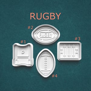 May include: Four white plastic cookie cutters with rugby-themed shapes. The shapes include a goal post, a football, a football with stitching, and a field. The word "RUGBY" is printed in orange at the top.