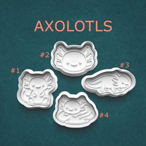 May include: Four white plastic cookie cutters shaped like axolotls, labeled #1 through #4. The text AXOLOTLS appears at the top. Each cutter features a distinct pose: a standing axolotl, a head-only design, a side-profile view, and a resting axolotl.
