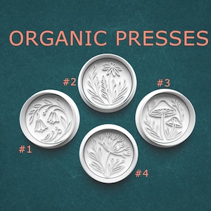 May include: Four white, circular organic presses with botanical designs, including flowers and mushrooms. The text "ORGANIC PRESSES" is in coral above the presses. Each press is labeled with a number.