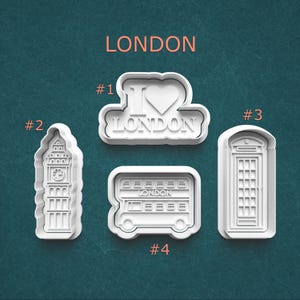 May include: Four white plastic cookie cutters with London-themed designs. Includes an "I Love London" design, Big Ben, a double-decker bus, and a red telephone box. The word "LONDON" is printed above the cutters.