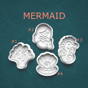 May include: Four white plastic cookie cutters in a mermaid theme. The cutters include a coral, a mermaid, a seahorse, and an open clam shell with a pearl. The word "MERMAID" is printed in orange at the top.