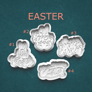 May include: Four white plastic Easter-themed cookie cutters. The cutters are in various shapes, including a bunny and egg shapes, with the words "Happy Easter" and the word "Easter" in orange. The cutters are numbered 1 through 4.