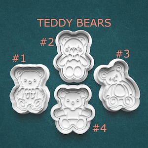 May include: Four white plastic teddy bear-shaped cookie cutters. Each cutter has a different design, with details like bows and overalls. The text "TEDDY BEARS" is above the cutters, with numbers identifying each design.