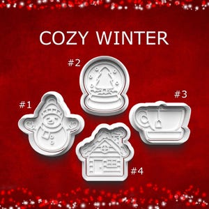 May include: White plastic cookie cutters in winter-themed shapes: a snowman, a snow globe with a tree, a teacup, and a house. The words "COZY WINTER" are above the cutters on a red background.