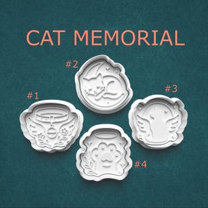 May include: White plastic cat memorial cookie cutters. The image shows four different designs: a cat collar with wings, a sleeping cat, a cat with angel wings, and a paw print with a halo. The text "CAT MEMORIAL" is at the top.
