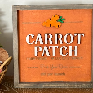 May include: Wooden sign with a gray frame and an orange background. The sign reads "CARROT PATCH" in white letters, with a carrot graphic at the top. The text "FARM FRESH & LOCALLY GROWN" is also visible.