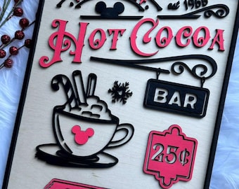Könnte beinhalten: Holzschild mit schwarzem Rahmen mit den Worten "Main Street" und "Hot Cocoa" in Pink. Enthält eine Tasse Kakao, einen Schneeflocke und ein Schild mit der Aufschrift "Bar". Das Schild sagt auch "Served Here" und "extra marshmallows".