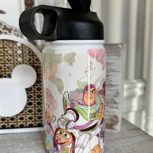 Puede incluir: Una botella de agua blanca con tapa negra y un dise&ntilde;o envolvente con personajes de la pel&iacute;cula de animaci&oacute;n Toy Story. La botella tiene una tapa abatible negra y un asa para facilitar su transporte.