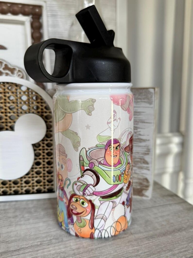 Puede incluir: Una botella de agua blanca con tapa negra y un dise&ntilde;o envolvente con personajes de la pel&iacute;cula de animaci&oacute;n Toy Story. La botella tiene una tapa abatible negra y un asa para facilitar su transporte.