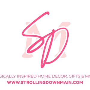 May include: A logo featuring the pink script letters SD overlaid on a pale pink letter M. Below the logo, the text reads MAGICALLY INSPIRED HOME DECOR, GIFTS & MORE followed by the website address WWW.STROLLINGDOWNMAIN.COM in pink capital letters.