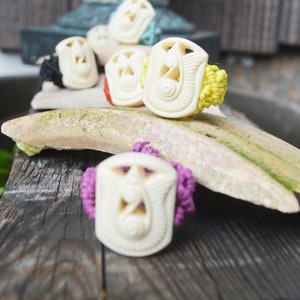 May include: Five white carved rings with intricate designs. The rings are tied with colourful cords in yellow, red and purple.