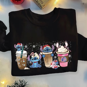 May include: Black sweatshirt with a Christmas-themed design featuring cartoon characters holding cups of coffee and hot chocolate. The characters are blue and have large eyes. The design includes snowflakes and the text "Cocoa".