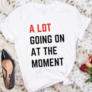 May include: White t-shirt with the text "A LOT GOING ON AT THE MOMENT" in black and red lettering.