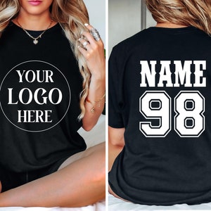 May include: Black t-shirt with a white circle on the front that says "YOUR LOGO HERE". The back of the shirt has white text that says "NAME 98".