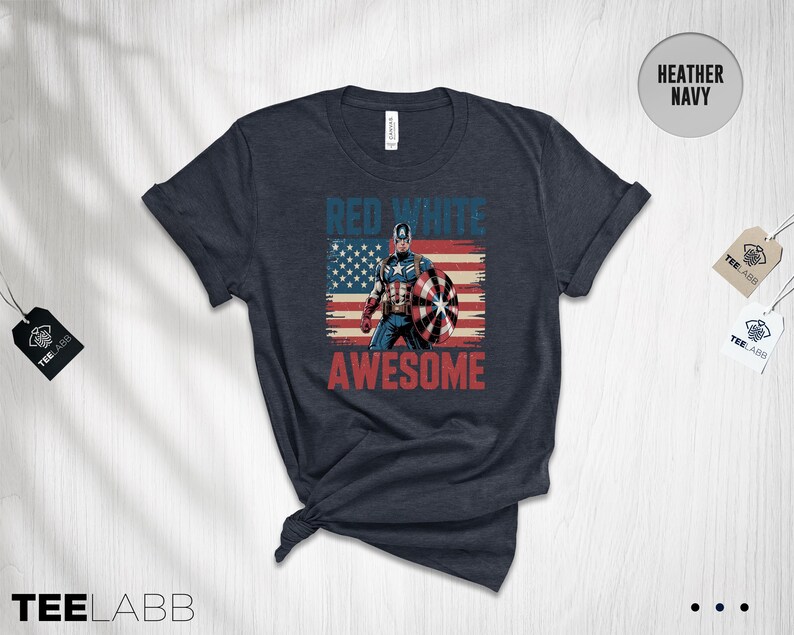 May include: A heather navy short-sleeve t-shirt featuring a graphic of Captain America standing in front of a distressed American flag. The text "RED WHITE" appears in blue above the character, and "AWESOME" is printed in red below the graphic.