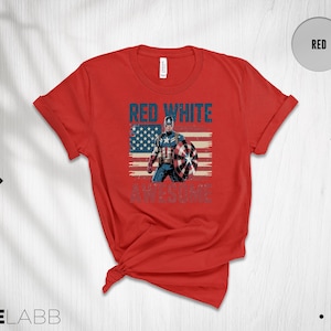 May include: A red short-sleeve t-shirt featuring a graphic of Captain America standing in front of a distressed American flag. The text "RED WHITE" appears in blue above the character, and the word "AWESOME" is printed in blue below.