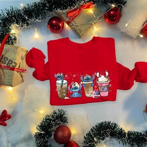 May include: Red Christmas sweater with a graphic of four Stitch characters holding different holiday drinks. The characters are wearing Santa hats and holding cups of coffee, hot chocolate, and eggnog.