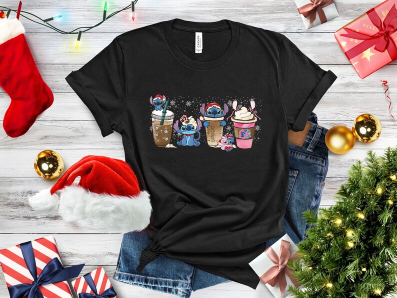May include: Black t-shirt with a graphic of four Stitch characters holding different holiday drinks. The characters are wearing Santa hats and holding cups of coffee, hot chocolate, and eggnog. The background is a white snowflake pattern.
