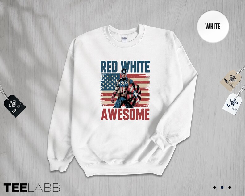 May include: A white crewneck sweatshirt featuring a graphic print of a superhero holding a shield in front of a distressed American flag. The text RED WHITE is printed in blue above the figure, and the word AWESOME is printed in red below.