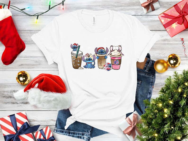 May include: White t-shirt with a graphic of four Stitch characters dressed as different holiday drinks. The characters are wearing Santa hats and holding cups of coffee, hot chocolate, and iced coffee.