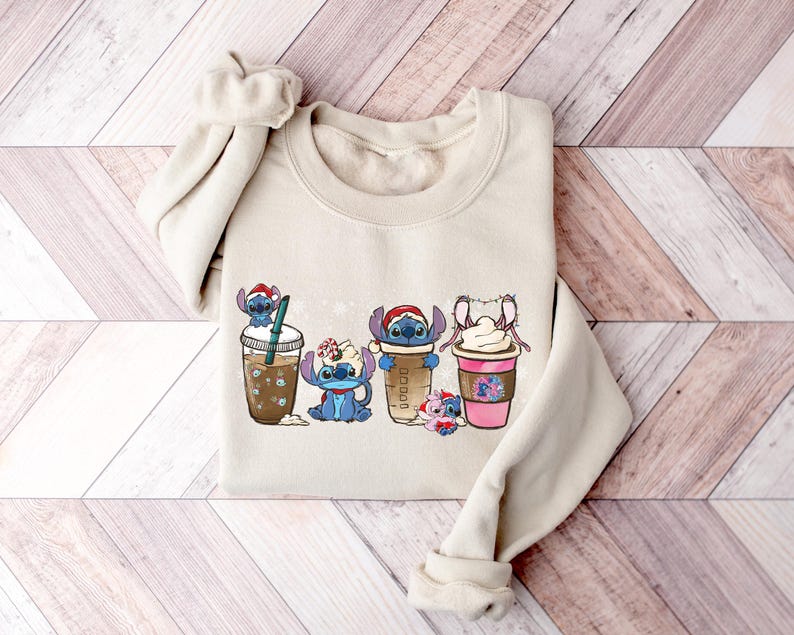 May include: A beige sweatshirt with a graphic print of four Stitch characters holding different coffee drinks. The characters are wearing Santa hats and holding cups with whipped cream and sprinkles.