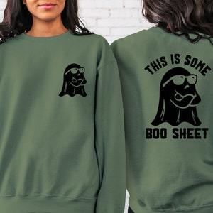 以下が含まれることがあります： 黒いサングラスをかけた黒い幽霊と「This is some boo sheet」という文字が背中に書かれた緑色のスウェットシャツ。スウェットシャツの前には、黒いサングラスをかけた小さな黒い幽霊が描かれている。