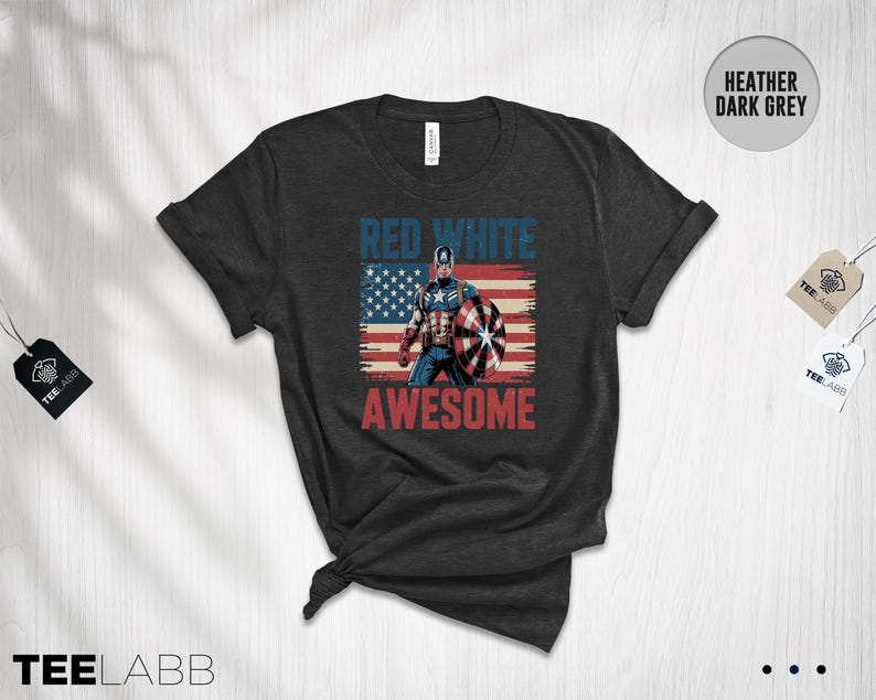 May include: A heather dark grey t-shirt featuring a graphic of a superhero holding a shield in front of a distressed American flag. The text "RED WHITE" appears in blue above the figure, and the word "AWESOME" is printed in red below the graphic.