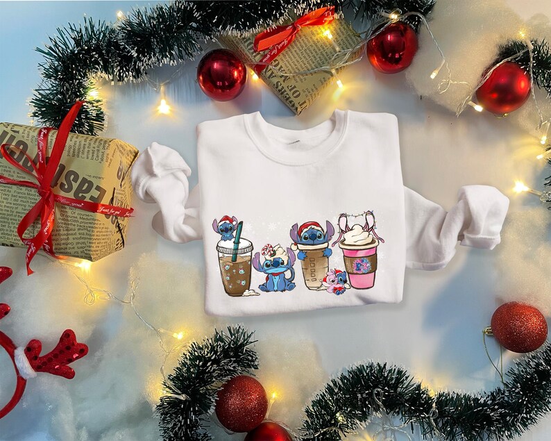 May include: White sweatshirt with a Christmas-themed design featuring Stitch characters holding cups of coffee and cocoa.