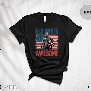 May include: A black short-sleeve t-shirt featuring a graphic of Captain America standing in front of a distressed American flag. The text RED WHITE is printed in blue above the character, and the word AWESOME is printed in red below the character.