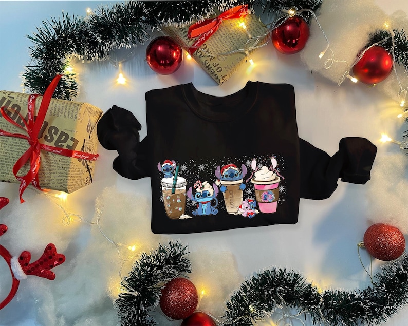 May include: Black sweatshirt with a Christmas-themed design featuring cartoon characters holding cups of coffee and hot chocolate. The characters are blue and have large eyes. The design includes snowflakes and the text "Cocoa".