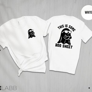 以下が含まれることがあります： 白いTシャツに、サングラスをかけた幽霊が描かれており、後ろには「This is some boo sheet」という文字が書かれています。Tシャツの前には、小さな幽霊のグラフィックが描かれています。