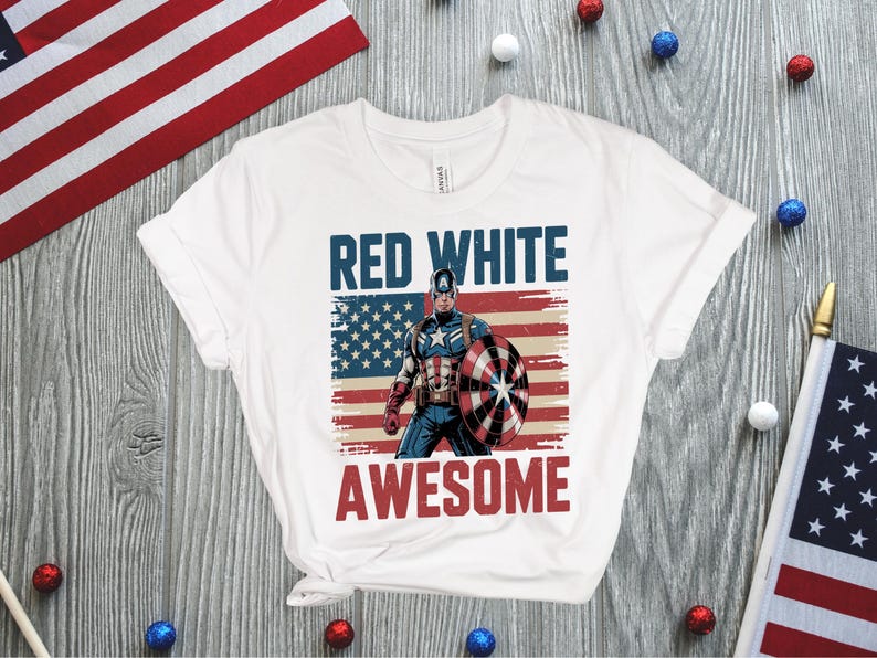 May include: A white short-sleeve t-shirt featuring a graphic of Captain America holding a shield in front of a distressed American flag. The text "RED WHITE" appears in blue above the character, and the word "AWESOME" is printed in red below.