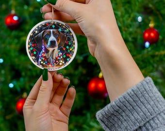 May include: A round white ceramic Christmas ornament with a photo of a brown and white dog wearing a string of colorful Christmas lights. The dog is looking directly at the camera.
