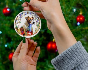 May include: A round white ceramic Christmas bauble featuring a colourful image of a dog wearing a string of Christmas lights. The bauble has a gold string for hanging.