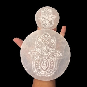 Könnte beinhalten: Zwei weiße Selenit-Untersetzer in Handform mit aufwendigen, geätzten Designs. Die Untersetzer sind rund, einer größer als der andere. Der Hintergrund ist schwarz.