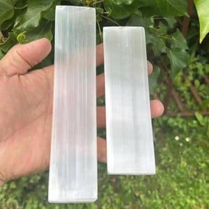 May include: Two white selenite sticks of different sizes. The sticks are smooth and have a natural, striated texture.