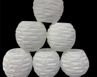 May include: Six white, spherical decorative vases with a textured, carved design. The vases are arranged in a pyramid shape against a black background. The vases are likely for home decor.