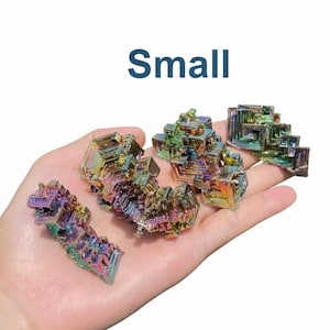 May include: A hand holding several small, iridescent bismuth crystals. The crystals display a range of colors, including blues, greens, yellows, and purples. The word "SMALL" is written in blue above the crystals.