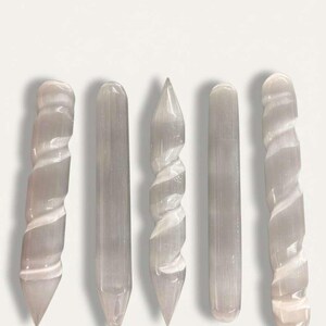 Può includere: Cinque bacchette di selenite di varie forme. Due bacchette hanno un design a spirale, due sono dritte e una ha una punta. Le bacchette sono di colore bianco sporco traslucido e sono disposte verticalmente su uno sfondo bianco.